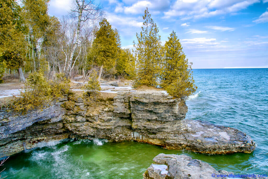 Cave Point County Park in Door County showing a rocky outcropping with trees and the wavy water below.