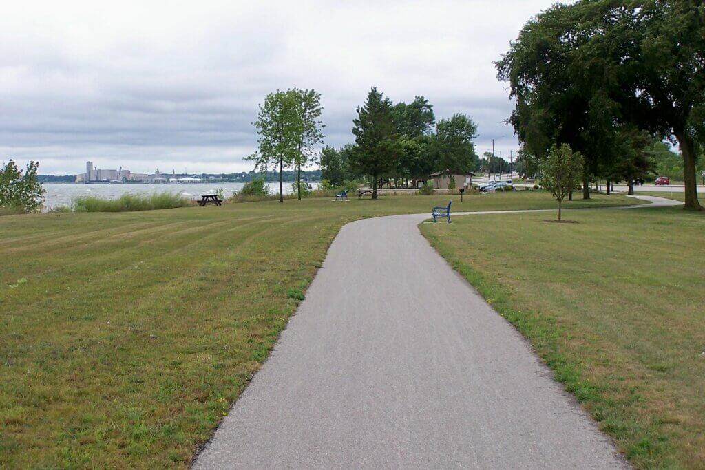 An empty bike path in Manitowoc with park benches and trees.