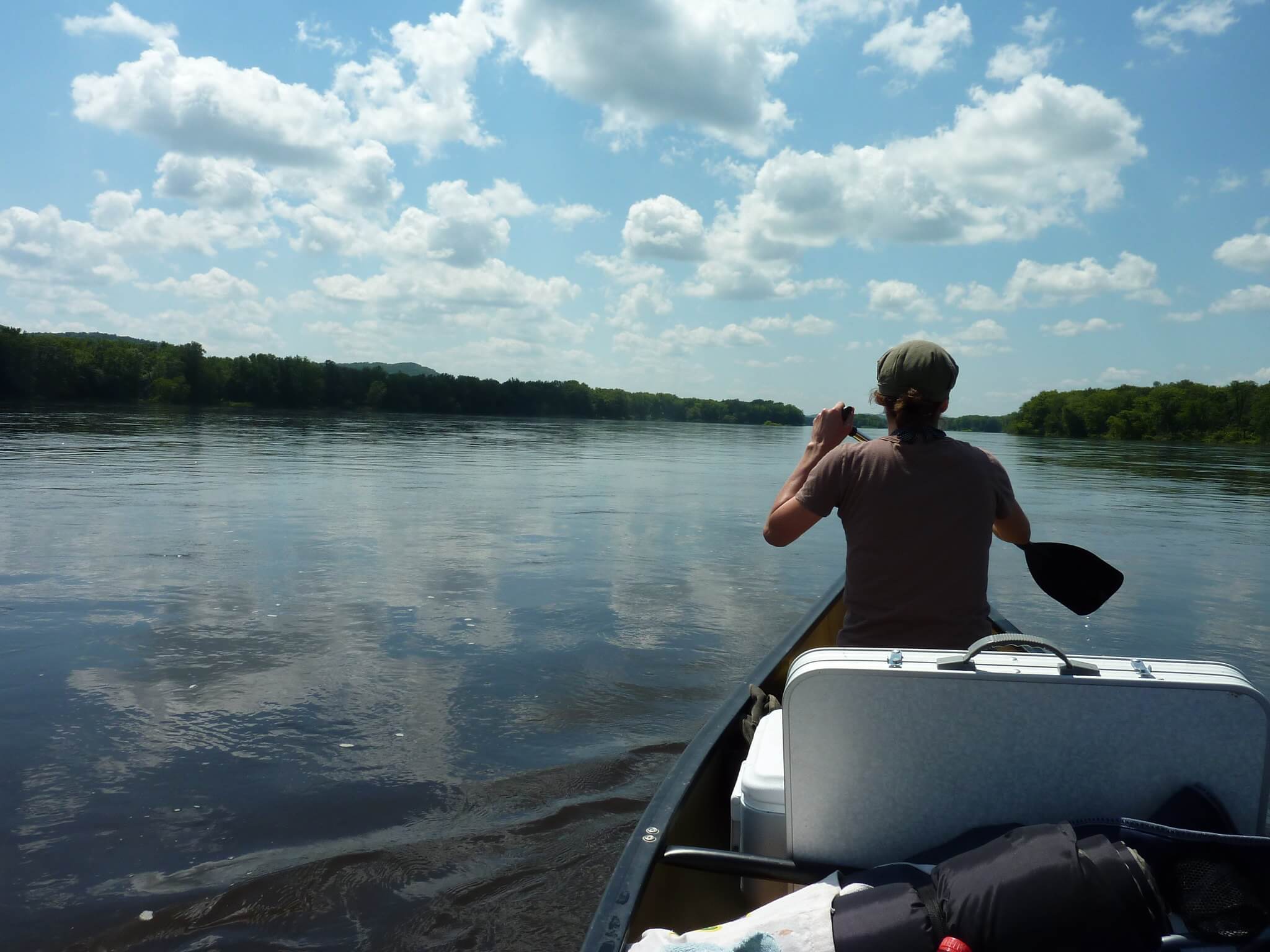 The back of a person canoeing on the Wisconsin River with a canoe filled with gear.