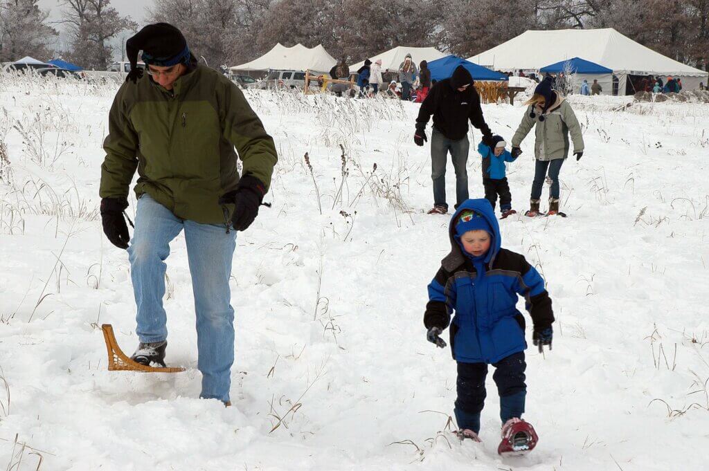 Families snowshoeing in Wisconsin with several white tents in the background.