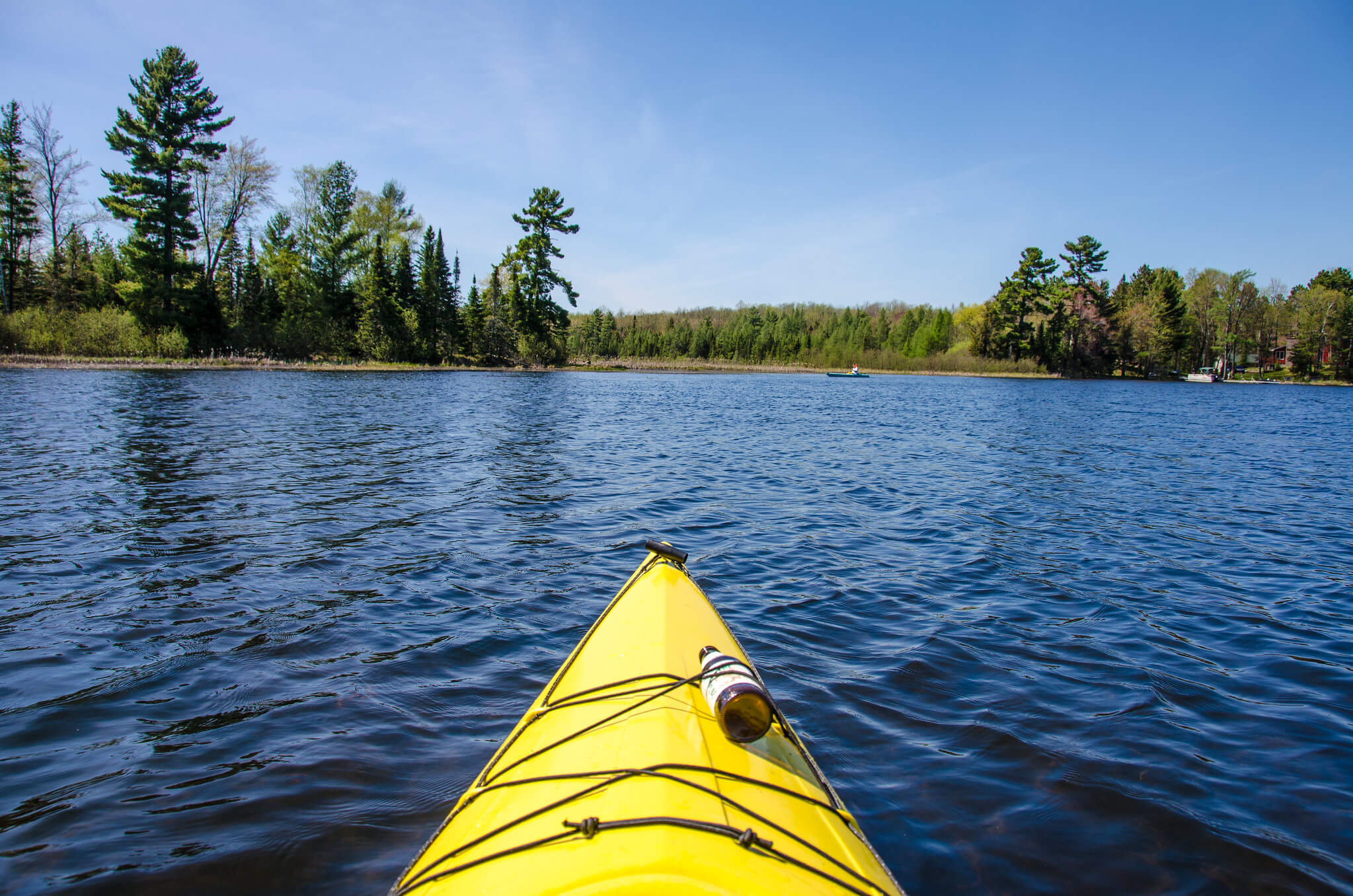 The yellow front tip of a kayak looking out over a deep blue Wisconsin lake with trees on the shoreline.