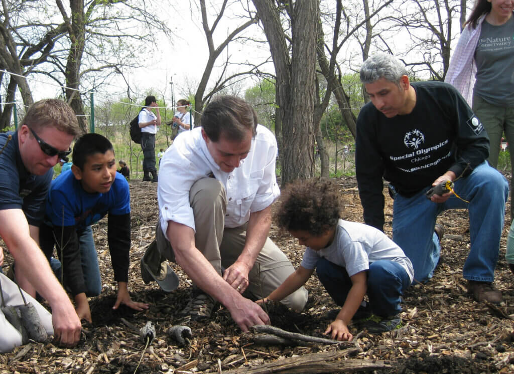 Adults helping kids plant trees.