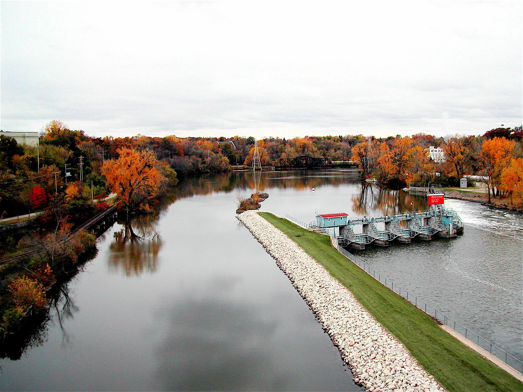 Fox River in Appleton, Wisconsin in the fall with a small manmade peninsula surrounded by trees changing color.