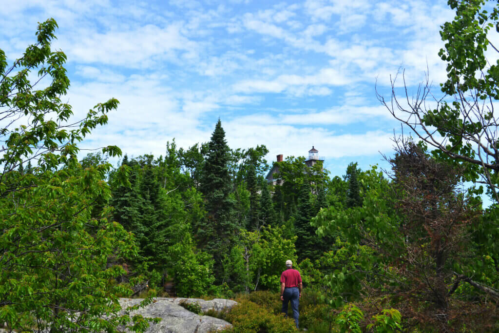 A man wearing a red shirt and jeans walking through a forest.