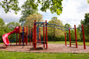 Knowles-Nelson Stewardship Program - red, blue, and yellow playground equipment in a small park surrounded by trees