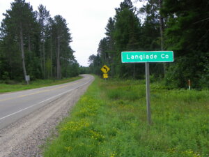 Knowles-Nelson Stewardship Program, Landglade County line road sign to the left of a road surrounded by tall trees and a grassy shoulder