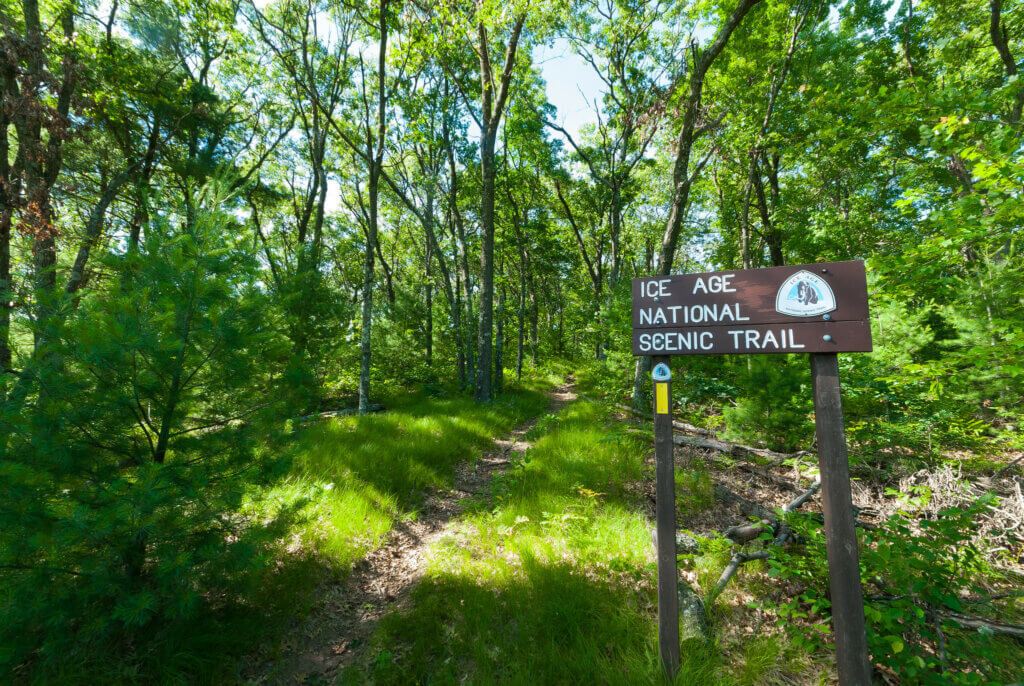 Knowles-Nelson Stewardship Program - a brown sign that reads Ice Age National Scenic Trail amidst a backdrop of a green wooded area