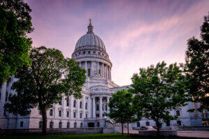 The Wisconsin state capitol building during summer with grassy lawn and green trees and a purple sky in early evening.