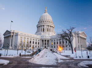 The Wisconsin state capitol building in winter with a large snow pile on the sidewalk in front of the building.