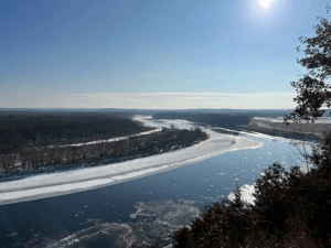 A birds eye view of a river that winds to the left along a frozen landscape with icy shorebanks,
