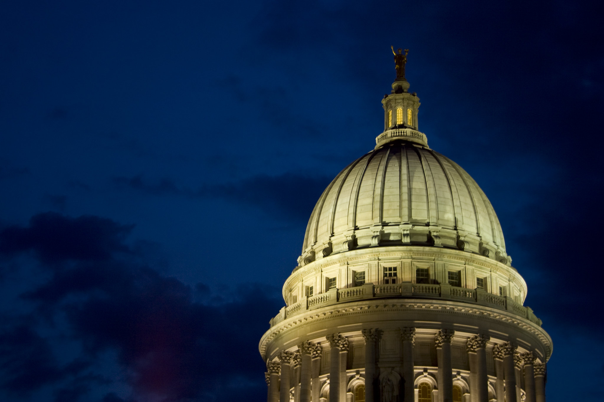 The dome of the Wisconsin state capital building lit up at night with a dark navy blue sky.