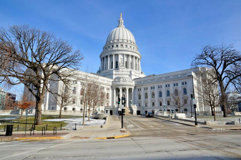 The Wisconsin State Capital building in spring with patches of snow on the ground and a cloudless blue sky.