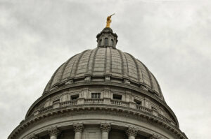 Close-up of exterior of rotunda of the Wisconsin Capitol building against a gray overcast sky.