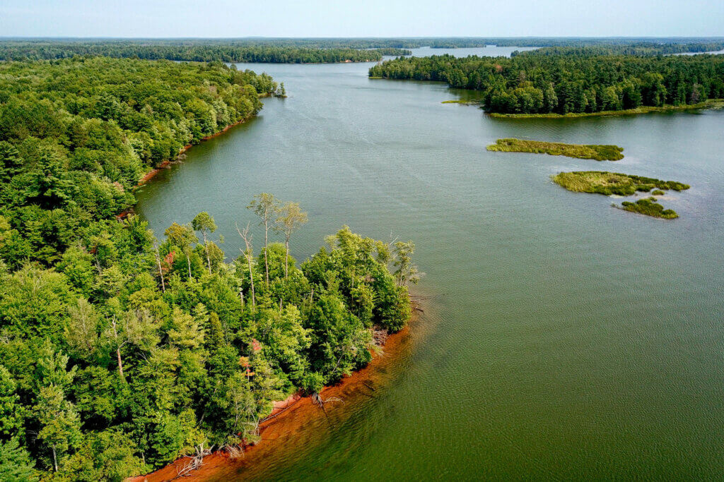 An aerial view of a large river flowage surrounded by green trees and dotted with small islands.