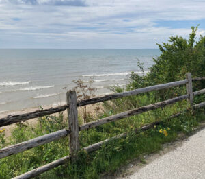 A weathered wooden fence with a view of Lake Michigan behind it. The sky is clear and blue.
