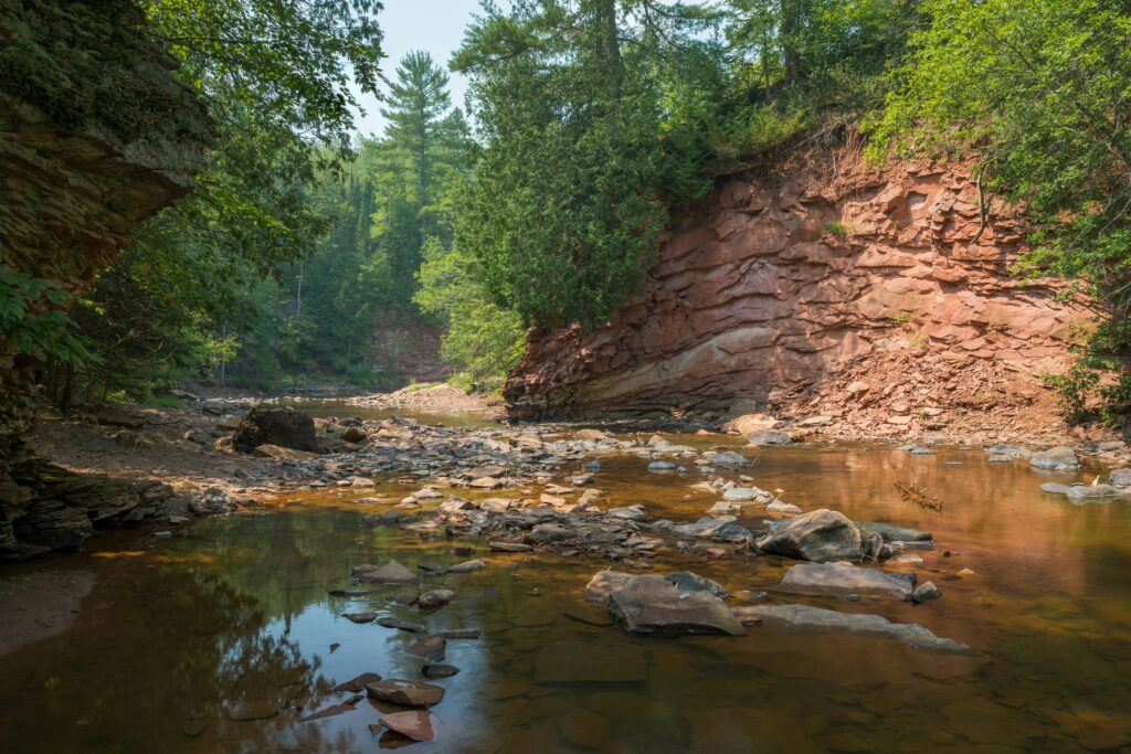 A river with steep red rock banks and trees.