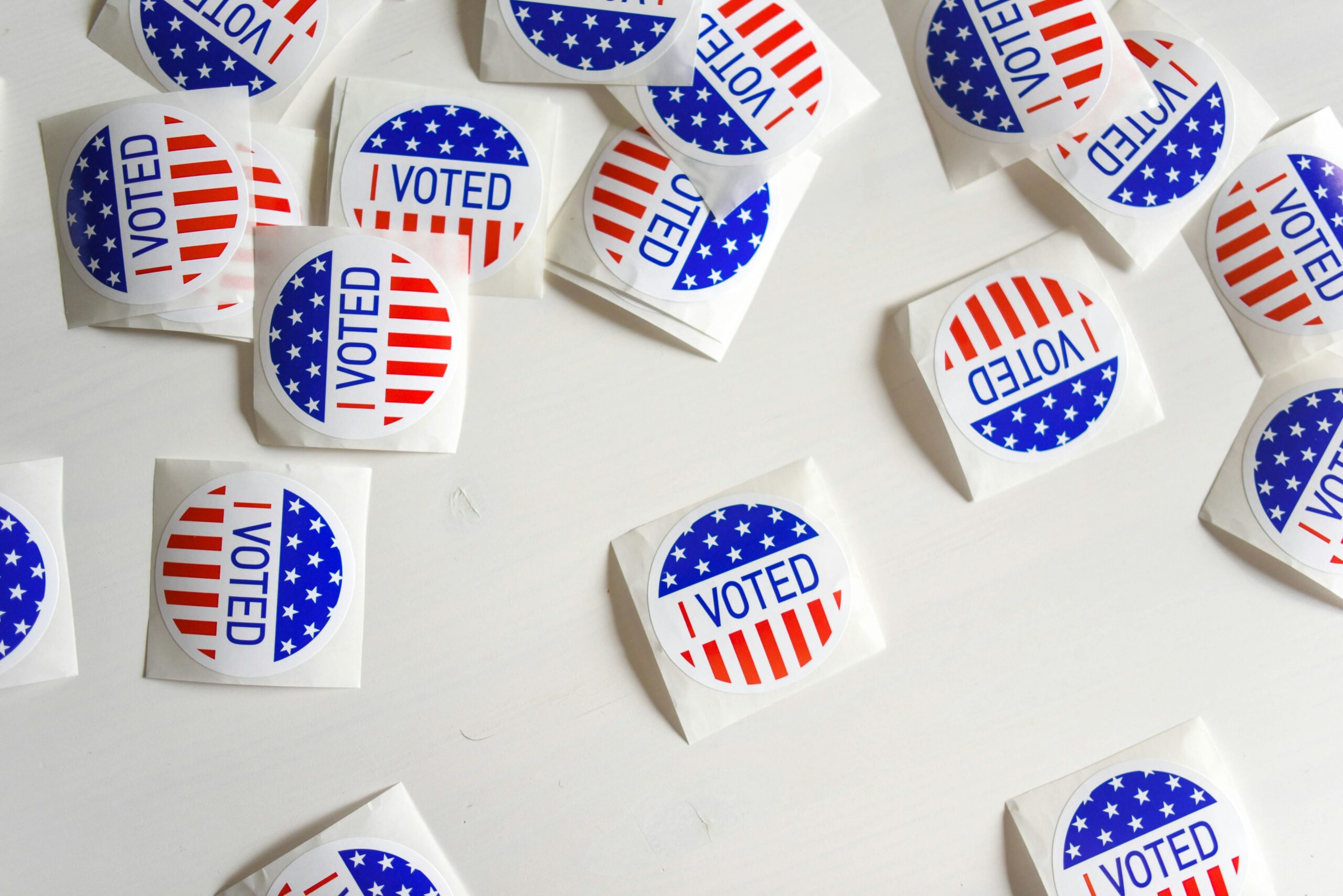 Several red white and blue 'I Voted" stickers scattered against a white backdrop.