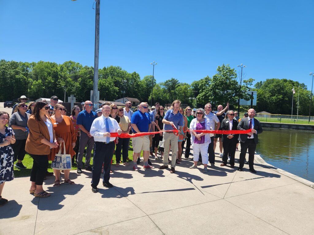 A group of adults standing near a riverfront park, celebrating a ribbon-cutting.