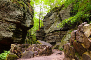 Large rock formations line a trail in a lush green woods.