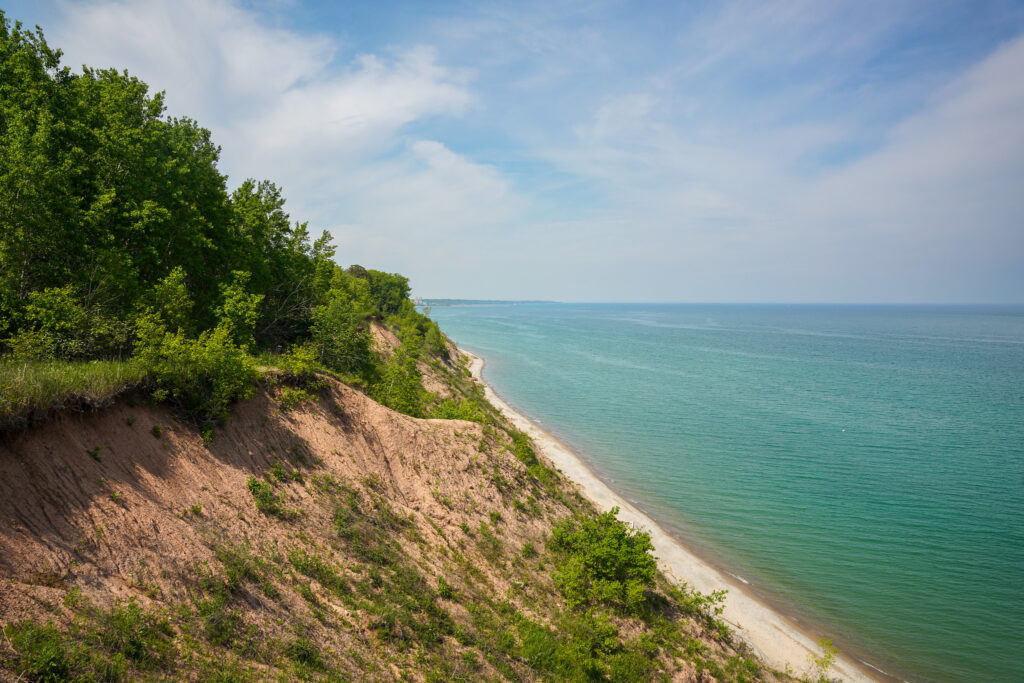 Steep, sandy bluff overlooking Lake Michigan, covered in green vegetation.