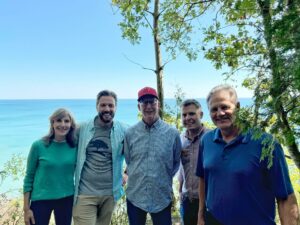 Five adults stand facing the camera with a scenic view of Lake Michigan in the background.