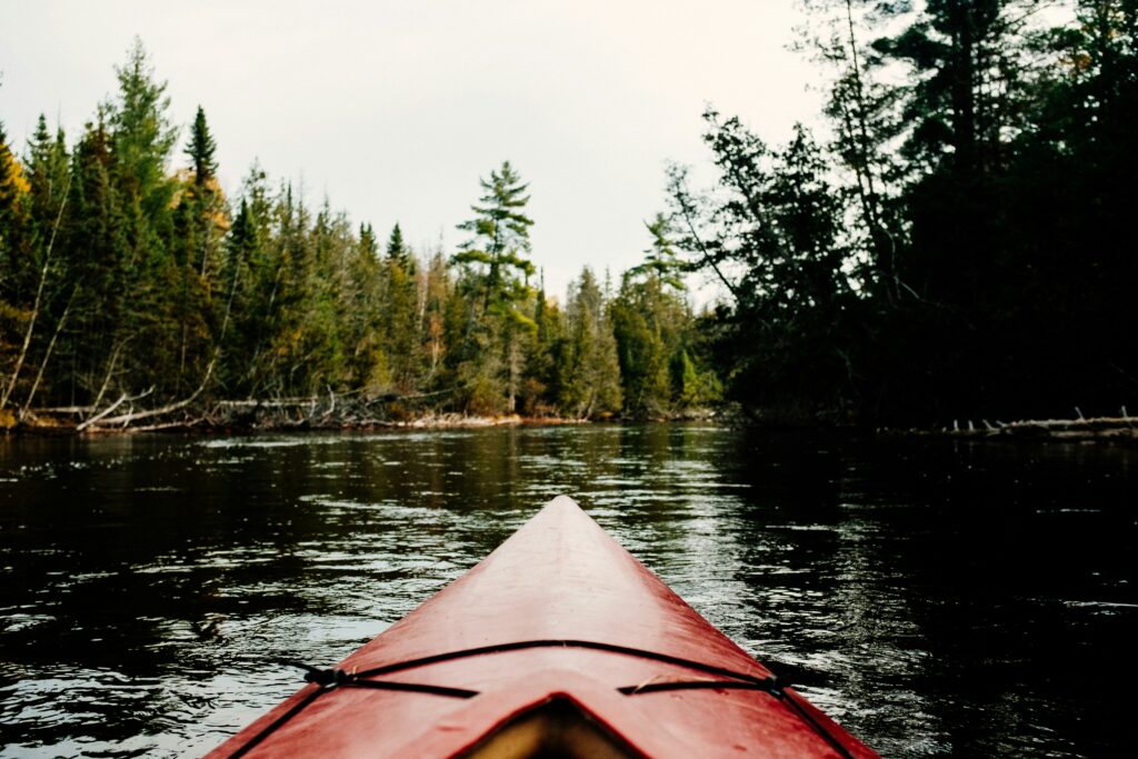 Bow of a red kayak on a tree-lined river.