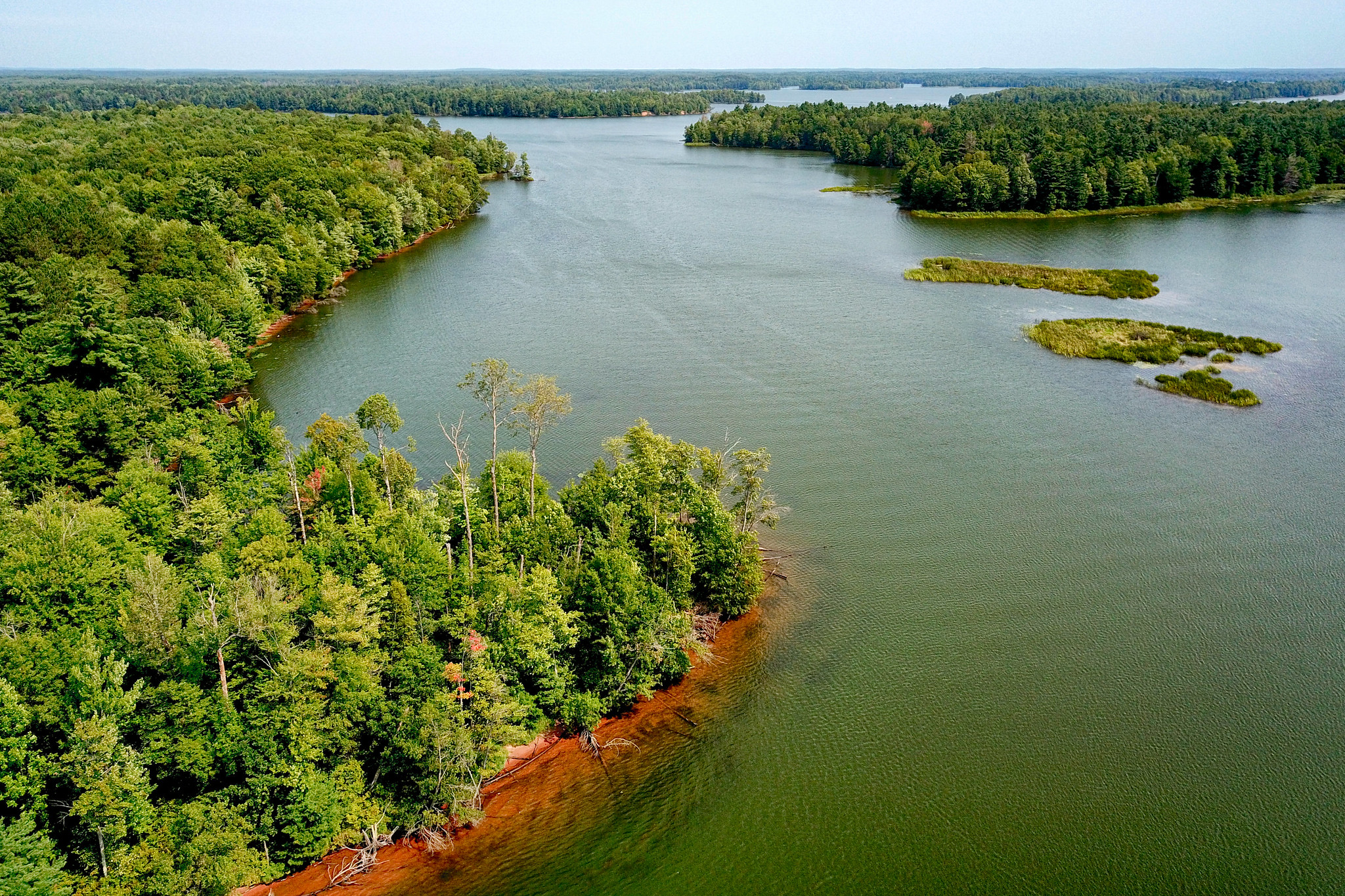 Aerial photo of a wide waterway lined with green vegetation and trees.