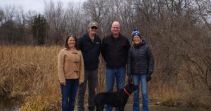 Four adults and a dog stand outside on an overcast fall day.