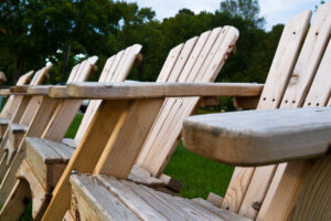 A close-up of Adirondack chairs lined up, with green trees in the background.