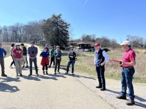 A group of adults in hiking clothing standing outside listening to a man speak.