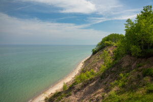 Steep, forested bluff overlooking a sandy beach and turquoise lake waters, with lush green vegetation covering the eroded slopes.