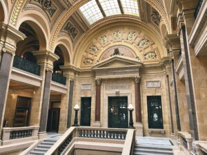 Grand staircase inside the Wisconsin capitol building with ornate architecture, decorative arches, marble columns, and detailed ceiling with skylights.