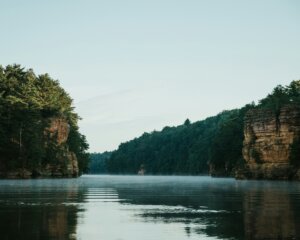 Green trees and bluffs line both sides of a river during daytime.