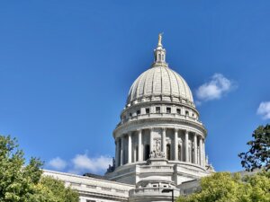 The Wisconsin State Capitol dome against a bright blue sky with white clouds.