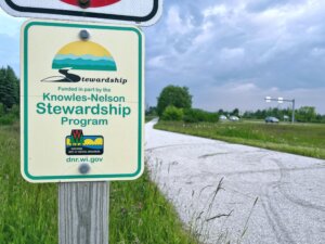 Knowles-Nelson Stewardship Program sign next to a trail and roadway.